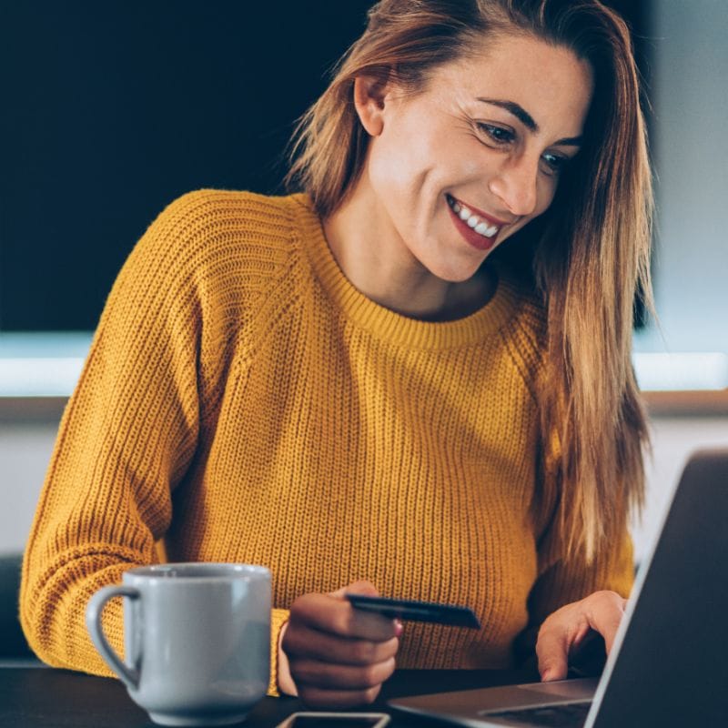 Woman in orange jumper paying on laptop with credit card